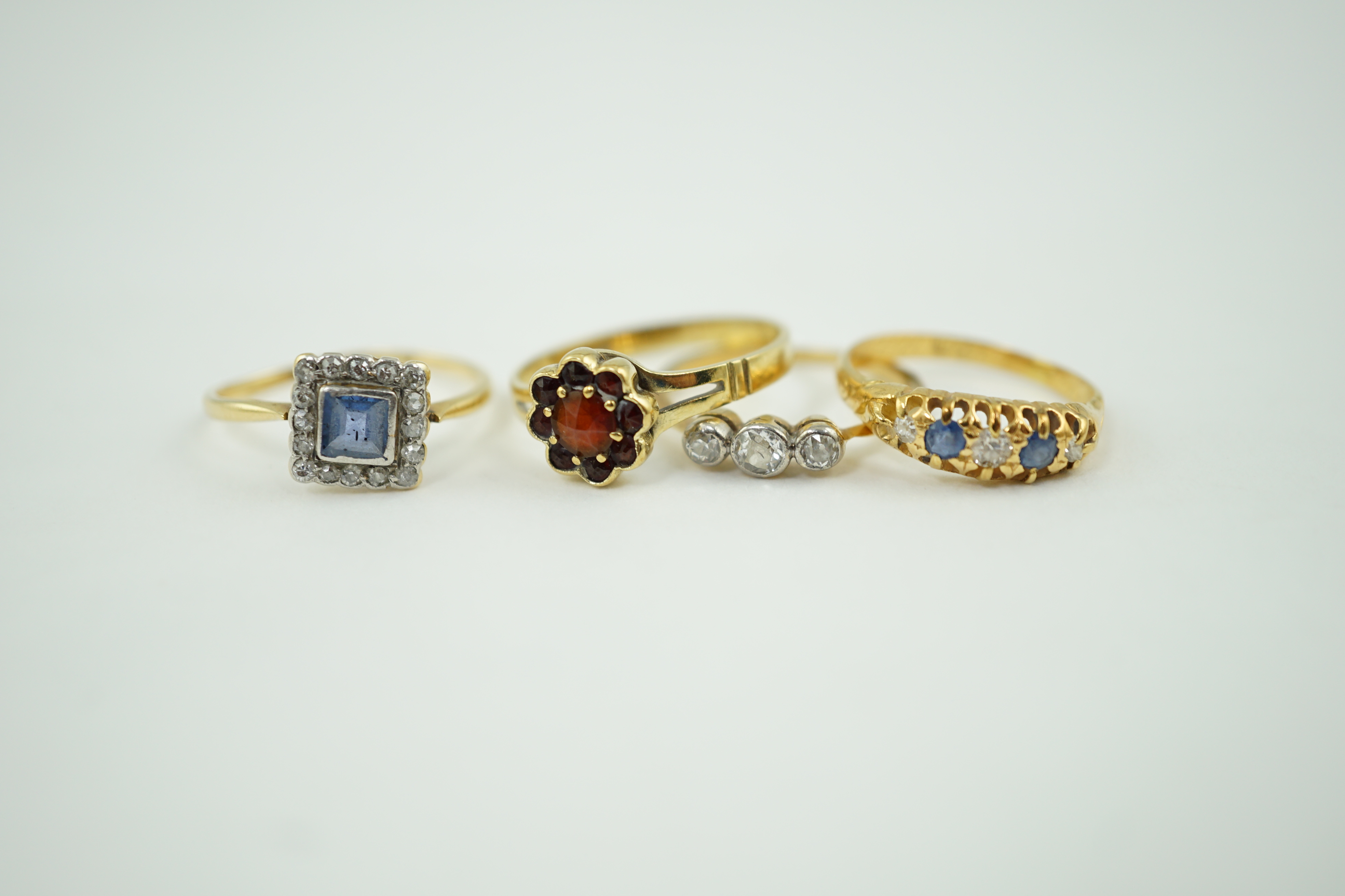 Four assorted rings including an 18ct gold, sapphire and diamond cluster set tablet ring, an 18ct sapphire and diamond half hoop, a gold and three stone diamond and a 14k gold and garnet cluster ring